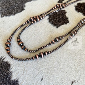 May include: A double strand necklace made of copper and black beads. The necklace is on a white and black cowhide background.