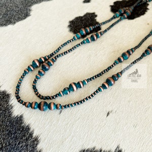 May include: A double strand necklace made of teal and copper colored beads. The necklace is on a white and black cowhide background.