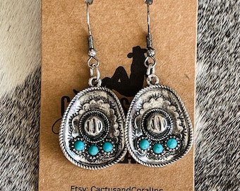 Pode incluir: Brincos de prata com um design de pedra turquesa. Os brincos têm a forma de uma ferradura e um design detalhado. Etsy: CactusandCoralInc IG: @cactusandcoralcountryboutique
