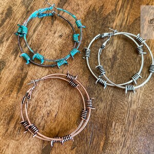 May include: Three pairs of hoop earrings with barbed wire accents. The earrings are in turquoise, silver, and rose gold.