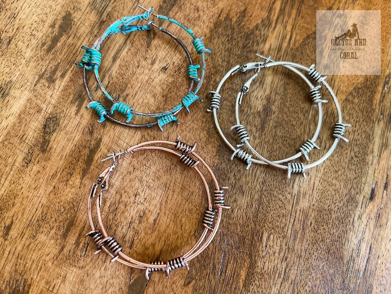 May include: Three pairs of hoop earrings with barbed wire accents. The earrings are in turquoise, silver, and rose gold.