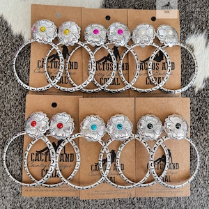 May include: Silver hoop earrings with a flower design and various colored stones. The earrings are displayed on cards with the text "Cactus and Coral Country Boutique".