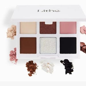 May include: A white eyeshadow palette with the word "Lithe" printed on the lid. The palette contains six eyeshadow shades in various colors, including beige, brown, pink, white, and black. Loose eyeshadow powder in matching colors is scattered around the palette.