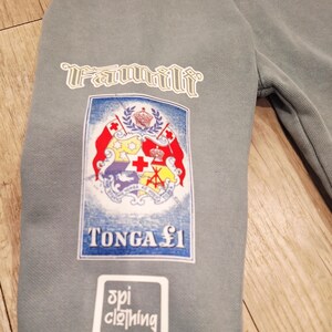 May include: A grey sweatshirt sleeve with three white patches. The top patch reads "Familii". The middle patch features a crest with red, white, and yellow elements. The bottom patch reads "spi clothing".