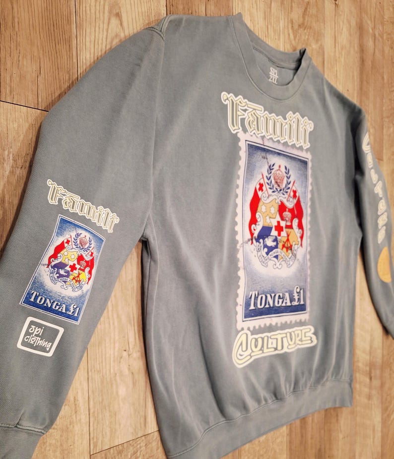 May include: A blue-grey sweatshirt with the word "Famili" in white script. The shirt features a postage stamp design with the words "TONGA &pound;1" and "CULTURE". The sleeve has a patch that says "api clothing".