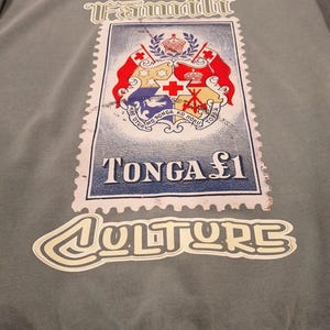 May include: Grey sweatshirt with a large Tonga stamp graphic. The stamp design includes a coat of arms and the text "TONGA &pound;1". The word "Culture" is written in a stylized font below the stamp.