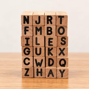 May include: A stack of twenty-four light brown wooden blocks arranged in a grid of four columns and six rows. Each block features a single black capital letter printed on the front face, including N, J, R, T, F, M, B, O, I, L, E, S, G, U, K, X, C, W, D, Q, Z, H, A, and Y.