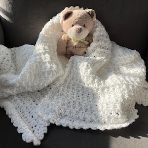 May include: White crocheted baby blanket with a scalloped edge. A brown teddy bear is sitting on top of the blanket.