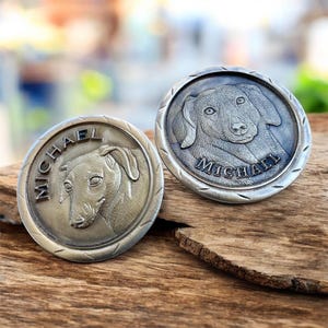 May include: Two round, silver-toned metal pet tags with a dog portrait and the name "MICHAEL" engraved around the edge. The tags are displayed on a wooden surface, showcasing the detailed relief of the dog's face.