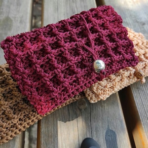 Puede incluir: Primer plano de tres bolsos de mano de ganchillo en tonos burdeos, beige y marrón. El bolso burdeos presenta un cierre de cuentas plateadas. Los bolsos están hechos con un patrón de puntada texturizada y se exhiben sobre una superficie de madera.