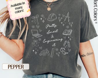 May include: A gray Comfort Colors t-shirt with the text "Pretty, Smart & Engineering it." surrounded by engineering-related doodles. The shirt is available in many colors. The shirt is pepper colored.