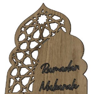 May include: Wooden Ramadan Mubarak decoration with a decorative cutout design. The top portion features a geometric pattern with star shapes. The words "Ramadan Mubarak" are written in a script font.