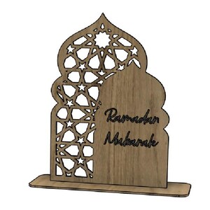 May include: Wooden Ramadan Mubarak decoration. The design features an arched shape with intricate star cutouts and the words "Ramadan Mubarak" in a script font. The base is rectangular, providing stability for the decorative piece.