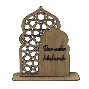 May include: A wooden Ramadan Mubarak decoration. The design features an arched shape with intricate star-shaped cutouts on the left side and the words "Ramadan Mubarak" on the right. The decoration is light brown and stands on a rectangular base.