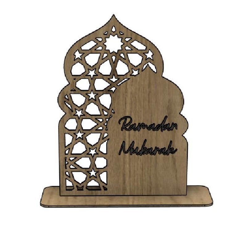 May include: A wooden Ramadan Mubarak decoration. The design features an arched shape with intricate star-shaped cutouts on the left side and the words "Ramadan Mubarak" on the right. The decoration is light brown and stands on a rectangular base.