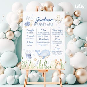 May include: A blue and white illustrated poster with the name "Jackson" and the text "My First Year". The poster lists the child's weight, height, favourite foods, songs, and activities. The poster is decorated with illustrations of a turtle, octopus, whale, jellyfish, and crab.