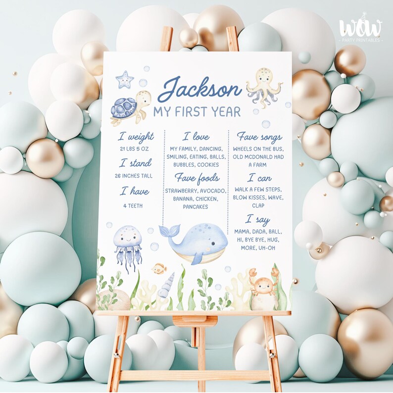 May include: A blue and white illustrated poster with the name "Jackson" and the text "My First Year". The poster lists the child's weight, height, favourite foods, songs, and activities. The poster is decorated with illustrations of a turtle, octopus, whale, jellyfish, and crab.