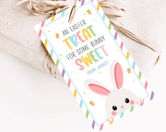 May include: Printable Easter gift tag featuring a white bunny with pink ears peeking out from behind a colorful striped border. The tag reads "An Easter Treat for some bunny Sweet" and includes space to personalize with a name. The tag measures 2 x 3.5 inches.