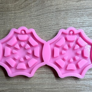 May include: A pair of pink, star-shaped silicone molds for crafting earrings or pendants. Each mold features a detailed geometric design with a small loop for attaching hardware. The molds are made of flexible, durable material.