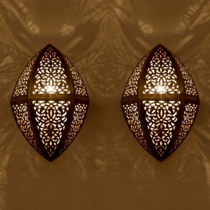 May include: Two ornate brass wall sconces with intricate cut-out designs. The sconces are illuminated from within, casting a warm glow.