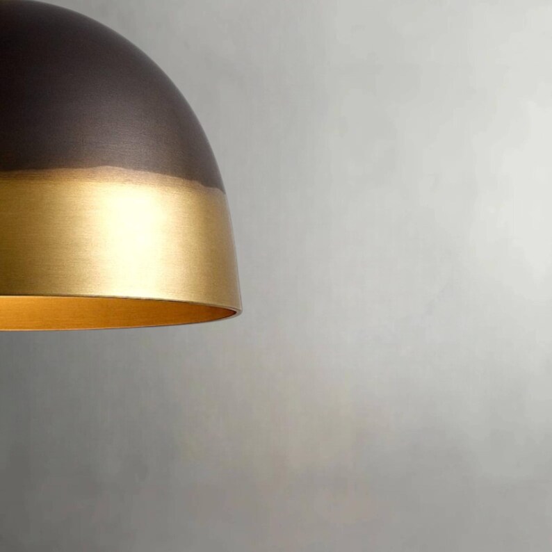 K&ouml;nnte beinhalten: Eine moderne Pendelleuchte mit zweifarbigem Design. Der obere Teil ist dunkelbronze, w&auml;hrend der untere Bereich eine goldene Oberfl&auml;che aufweist. Die Leuchte hat eine abgerundete, kuppelf&ouml;rmige Form, und der Innenraum ist ebenfalls goldfarben.