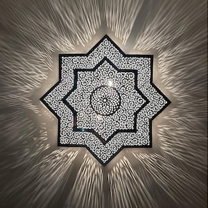 Può includere: Lampada decorativa a forma di stella, bianca e nera. L'intricato design geometrico proietta un motivo di luce radiale sulla parete. Un elemento di arredo casa unico ed elegante.