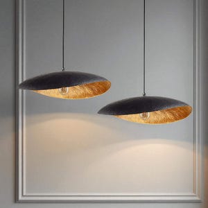 May include: Two pendant lights with a black, textured exterior and a gold-colored interior. The lights are suspended from the ceiling by thin black cords. The lampshades have a unique, organic shape, and the light bulbs are visible.