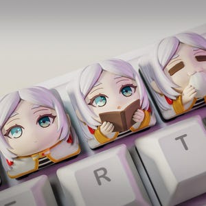 Könnte beinhalten: Nahaufnahme einer weißen Tastatur mit individuellen Tastenkappen, die Anime-Charaktere zeigen. Die Tastenkappen zeigen ein Mädchen mit weißen Haaren und blauen Augen in verschiedenen Posen, darunter Lesen und Trinken. Das Logo "nom nom Figures" ist sichtbar.