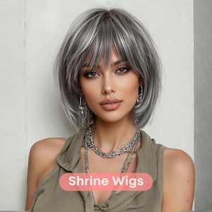 Könnte beinhalten: Eine Frau mit einer kurzen, gestuften Perücke in Grau- und Weißtönen. Die Perücke hat einen Pony und ist als Bob gestylt. Sie trägt ein grünes Oberteil und Silberschmuck. Der Text "Shrine Wigs" ist sichtbar.