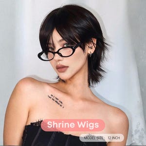 Puede incluir: Una persona con una peluca corta de color marrón oscuro con un estilo en capas y gafas ovaladas negras. La imagen incluye el texto "Shrine Wigs" y "Model Size: 30 cm".