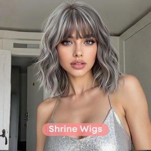 May include: A woman with a silver sequined top and a short, wavy gray wig with bangs. The wig has a natural look with highlights. The text "Shrine Wigs" is displayed on a pink oval.