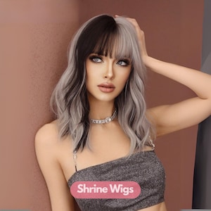 Op de afbeelding: Een vrouw met een tweekleurige pruik, zwart aan de ene kant en grijs aan de andere kant, met pony. Ze draagt een sprankelende top en een met juwelen bezette choker. De tekst "Shrine Wigs" is zichtbaar.