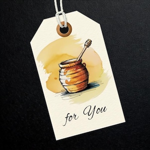 May include: A cream-colored gift tag with a watercolor illustration of a honey pot and dipper. The tag has the words "for You" in a script font. The background is a dark surface.