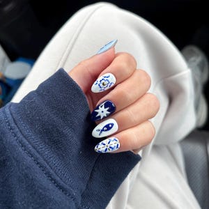 May include: Close-up of a hand with blue and white nail polish. The nails are decorated with a blue and white floral pattern.