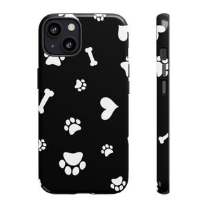 May include: Black phone case featuring a repeating pattern of white paw prints, bones, and hearts. The case has a glossy finish and a camera cutout on the back. The side view shows the case's thickness and button placement.