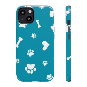 May include: A teal phone case featuring a pattern of white paw prints, hearts, and dog bones. The case has a black camera lens and button details. The side view shows the case's thickness and the continuation of the pattern.