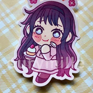 May include: A pink sticker featuring a cartoon girl with long, dark purple hair and large eyes. She wears a pink dress and holds a small cake. The sticker has a white border and flower accents.