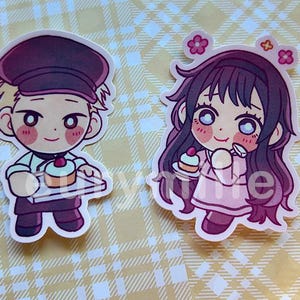 May include: Two cartoon stickers featuring characters holding cupcakes. One character is a male baker in a maroon cap and apron. The other is a female character with long dark hair and pink dress, with flowers in her hair.