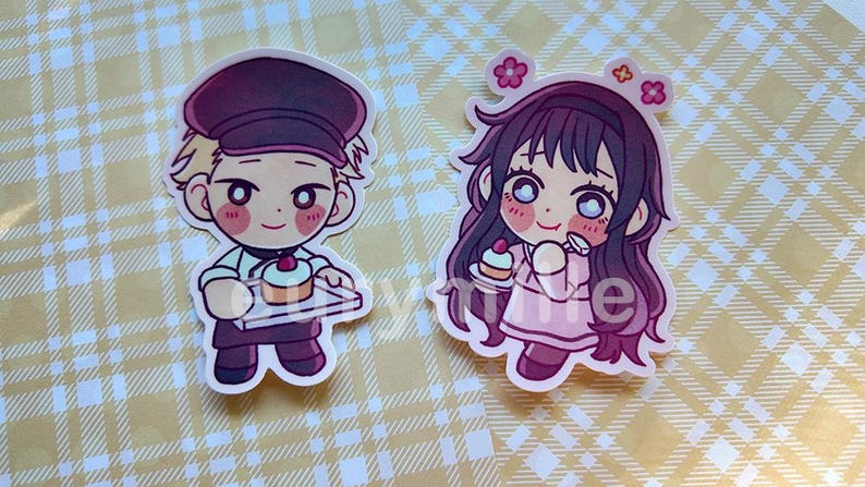 May include: Two cartoon stickers featuring characters holding cupcakes. One character is a male baker in a maroon cap and apron. The other is a female character with long dark hair and pink dress, with flowers in her hair.