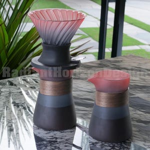 May include: A black and grey glass coffee carafe with a wooden band and a matching glass jug with a wooden band. The carafe has a glass filter with a pink and grey gradient.
