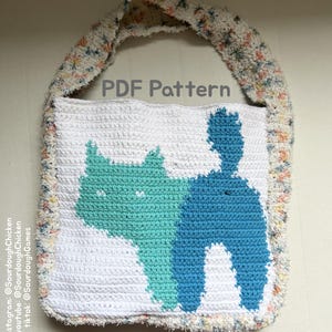 May include: A white crocheted tote bag with a blue and teal cat design. The bag has a fluffy, colorful strap. The text "PDF Pattern" is printed on the bag.