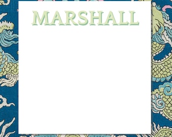 May include: A white notepad with the name "MARSHALL" in light green letters. The notepad is surrounded by a blue fabric with a dragon pattern in shades of green, blue, and pink.