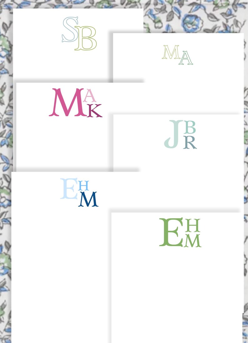 May include: A collection of personalized stationery cards with various monogram designs. The cards feature initials in different colors, including pink, blue, and green, set against a white background. The background has a floral pattern.