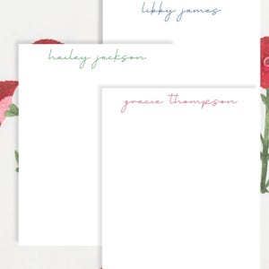 May include: Three white notepads with personalized names in different colors: "Libby James" in blue, "Hailey Jackson" in green, and "Gracie Thompson" in pink. The notepads are set against a floral patterned background.