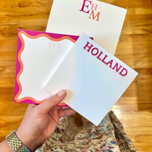 May include: Three personalized stationery sets with white paper and pink accents. One set features the initials "EM", another reads "HOLLAND", and the third has the name "EVA". The stationery has a modern, feminine design.