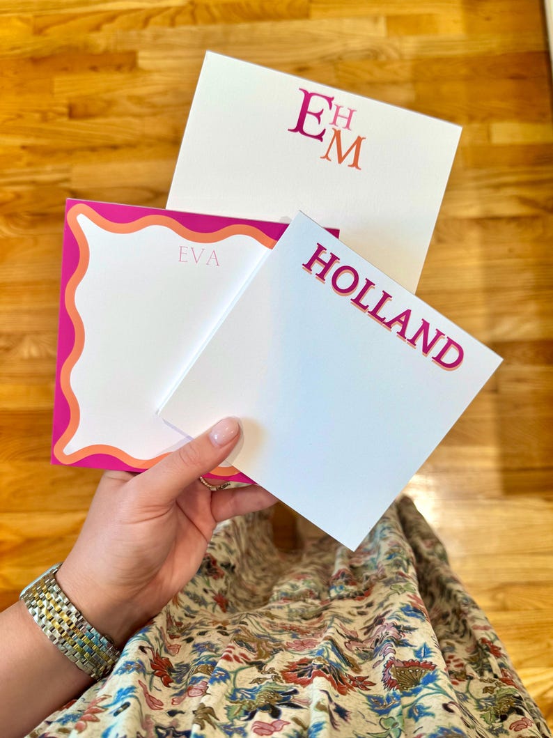 May include: Three personalized stationery sets with white paper and pink accents. One set features the initials "EM", another reads "HOLLAND", and the third has the name "EVA". The stationery has a modern, feminine design.