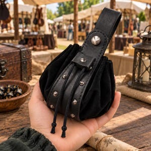 Puede incluir: Una bolsa de ante negro con cordón, que presenta una correa de cuero liso con tachuelas de metal plateado y un cierre de botón a presión a juego. La bolsa incluye una larga tira de cuero para colgar y dos cordones negros con extremos anudados.