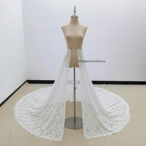 May include: A white lace bridal skirt with a long train is displayed on a mannequin. The skirt features a delicate floral lace pattern and a scalloped edge. The text "MettaCreations" is visible on the right side.