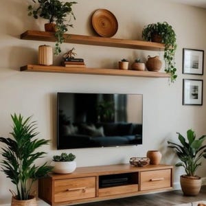 May include: A modern living room with a floating wooden TV stand and shelves. The shelves display plants, books, and decorative items. A large flat-screen TV is mounted above the stand, and potted plants are placed around the room.