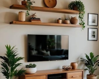 May include: Two horizontal wooden floating shelves mounted above a flat-screen television, which is positioned over a long, wall-mounted wooden media console with two drawers and a central open compartment, all decorated with various potted plants.